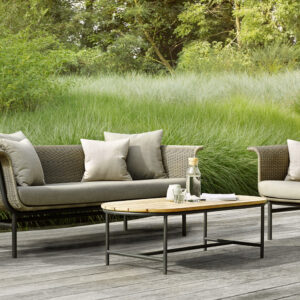 Outadore Space outdoor sofa and armchair set with neutral cushions placed on a wooden deck beside tall green grass